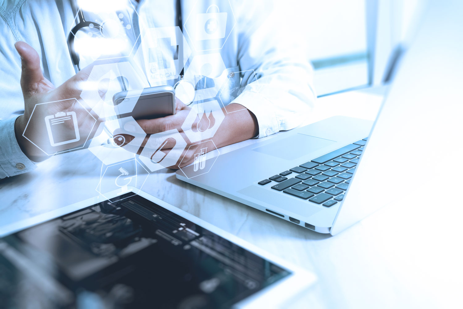 Doctor sitting at desk with laptop and tablet